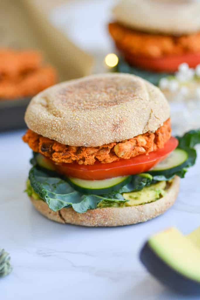 close up of a buffalo chickpea veggie burger on an eglish muffin with avocado, tomato and kale