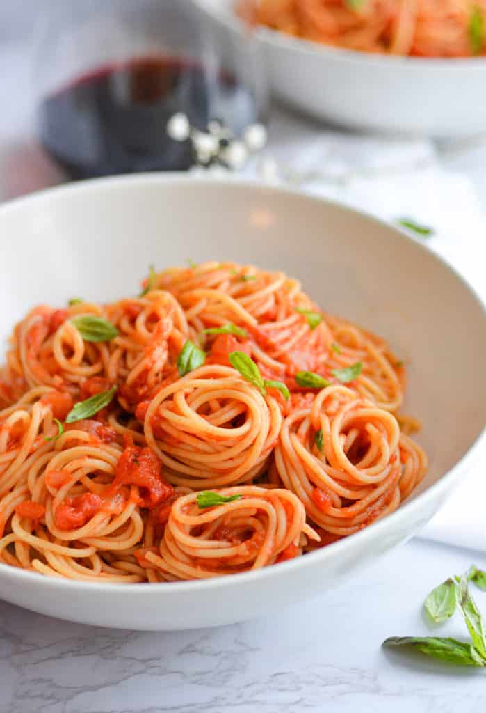 Lanscape of spaghetti with tomato sauce in a white bowl topped with basil