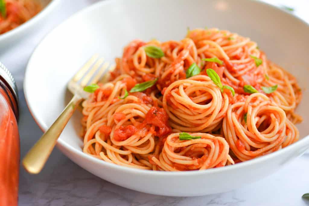 Lanscape of spaghetti with marinara sauce in a white bowl topped with basil