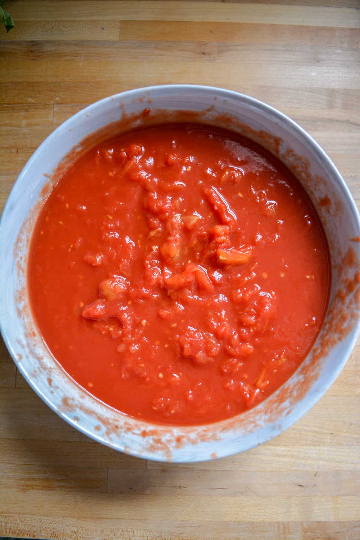 Crushed tomatoes in a large bowl on a wooden surface.