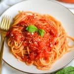Vegan Hearty Marinara Sauce on top of spaghetti on a plate with a gold fork to the left side.