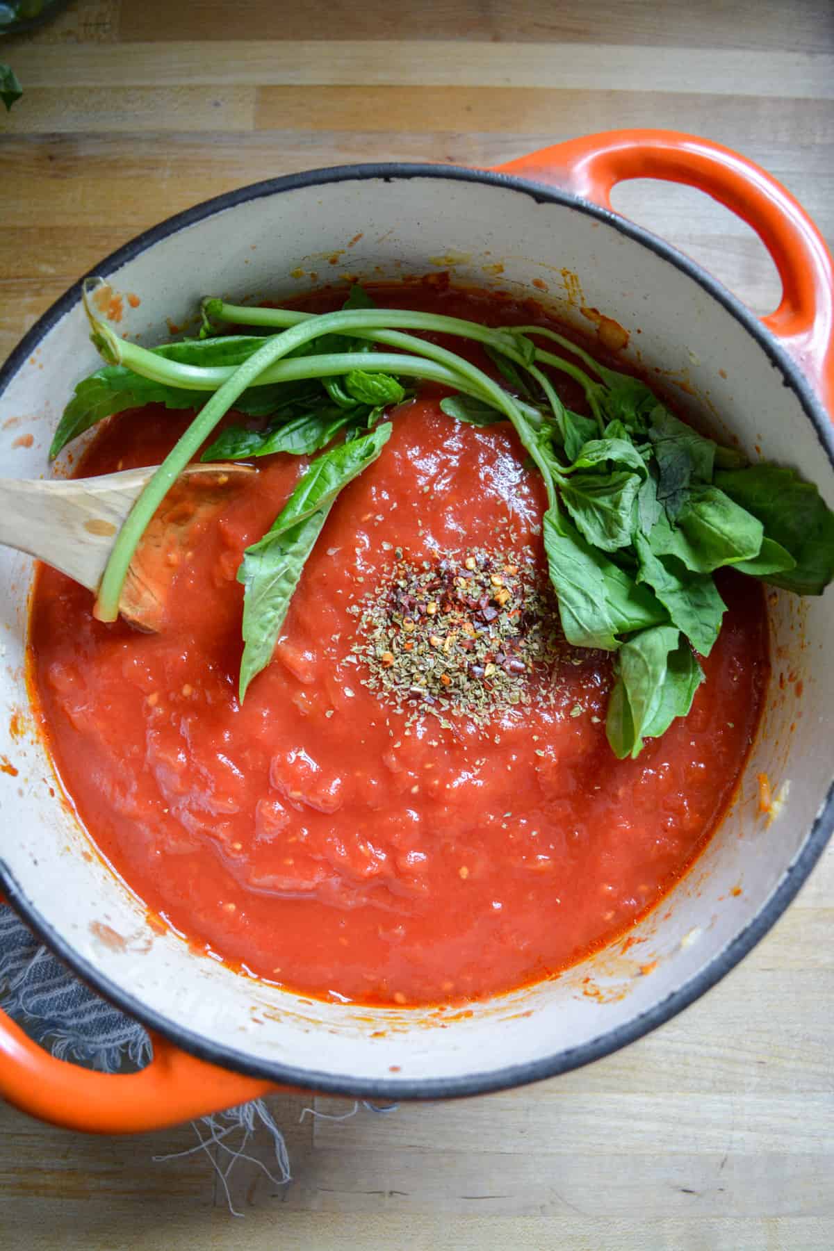 Tomatoes added into the the dutch oven topped with herbs and basil sprigs.