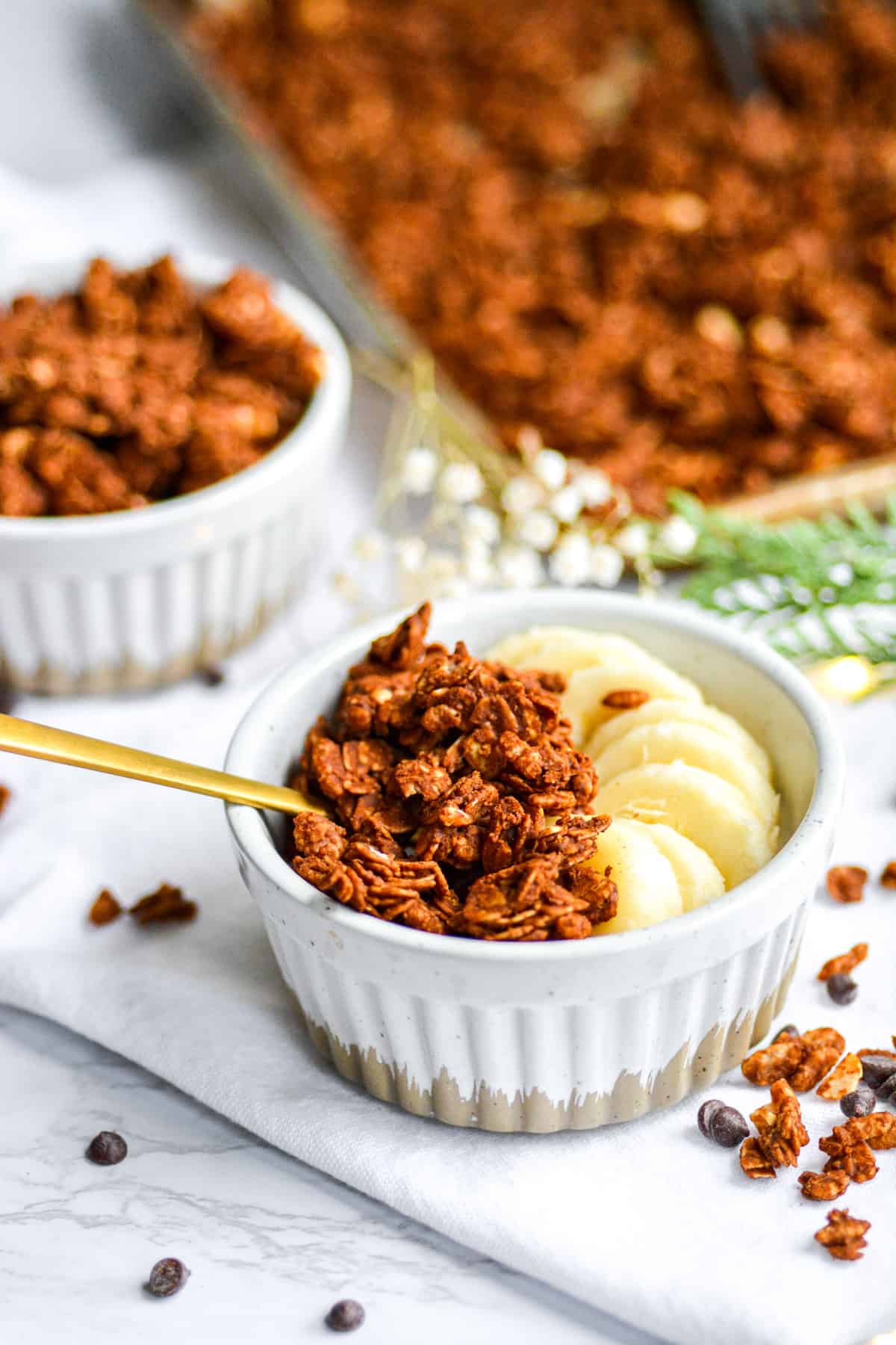 A ramekin with oil free chocolate peanut butter granola clusters and sliced banana