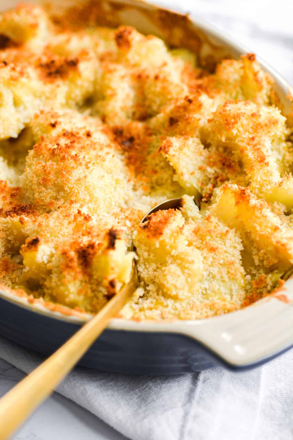 Vegan baked Cauliflower Gratin in a casserole dish with a gold spoon in it.