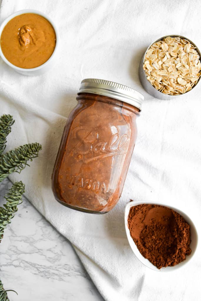 A mason jar next to cocoa powder and a cup of peanut butter