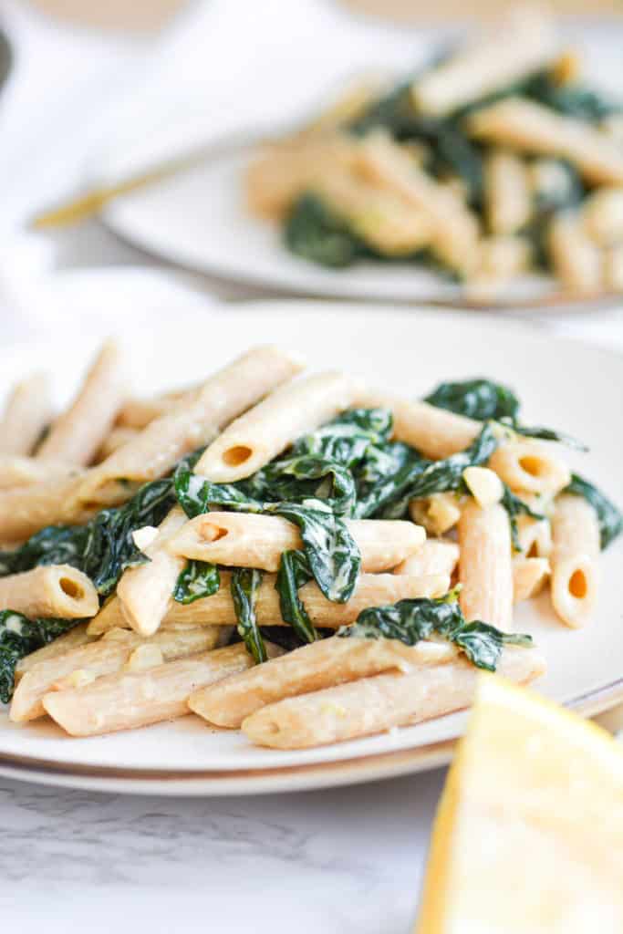 Two plates of creamy garlic pasta with kale on a marble board