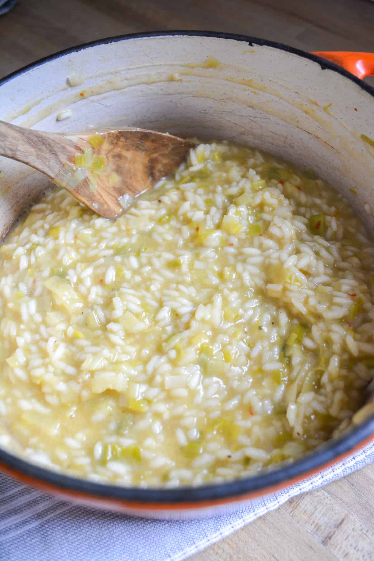 Finished Vegan Leek Risotto in a Dutch oven with a wooden spoon toward the back. 