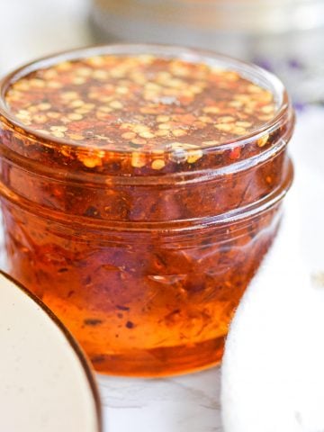Small glass jar full of hot honey next to 2 tan plates
