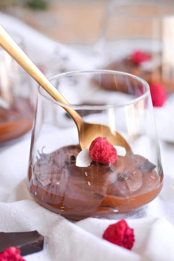 chocolate mousse garnished with a coconut flake and a raspberry with a gold spoon