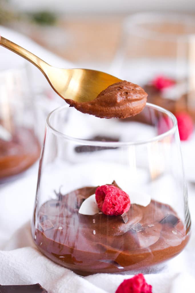 One ingredient chocolate mousse on a a gold spoon with glasses of chocolate mousse in the background