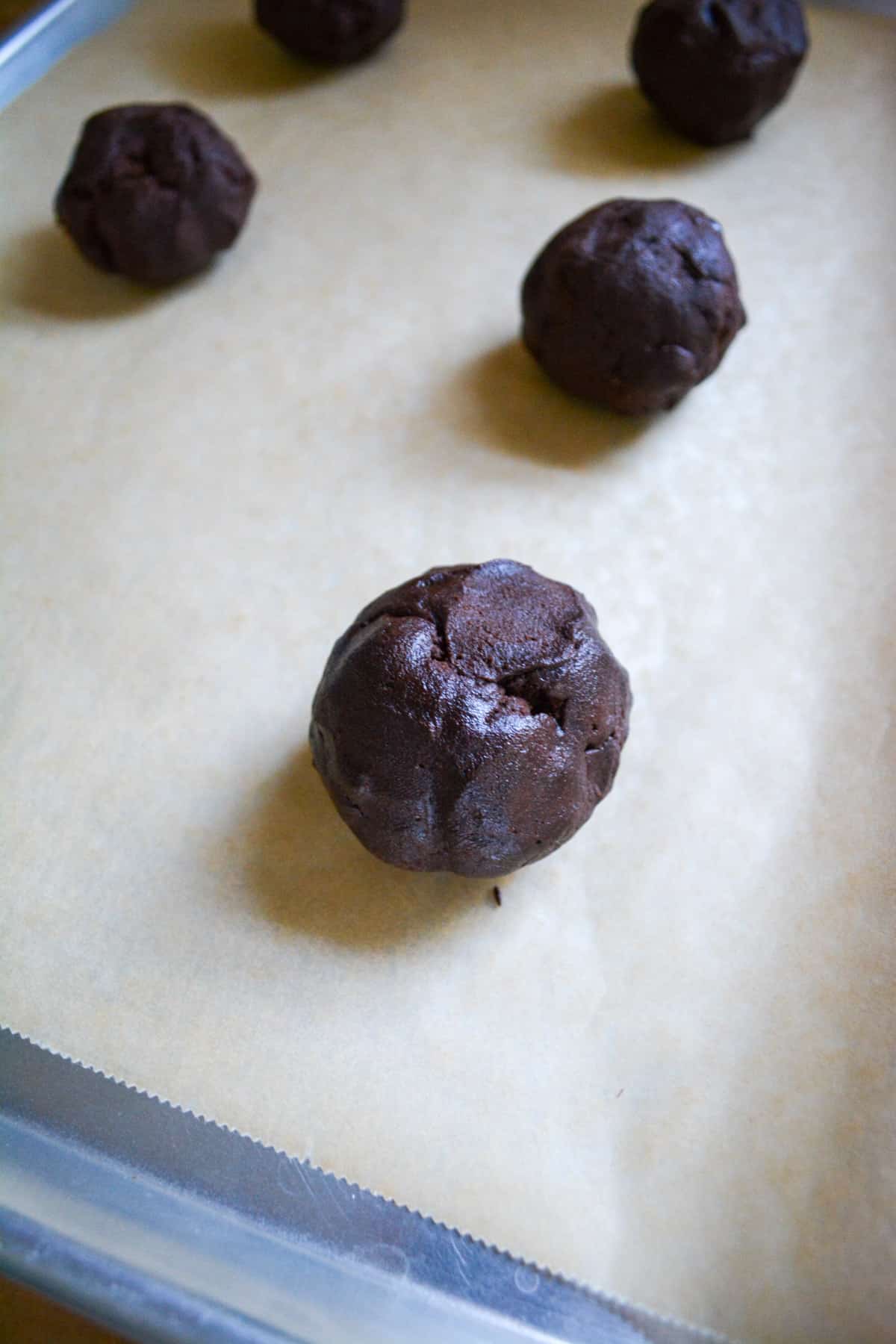 Chocolate dough balls on a baking sheet.