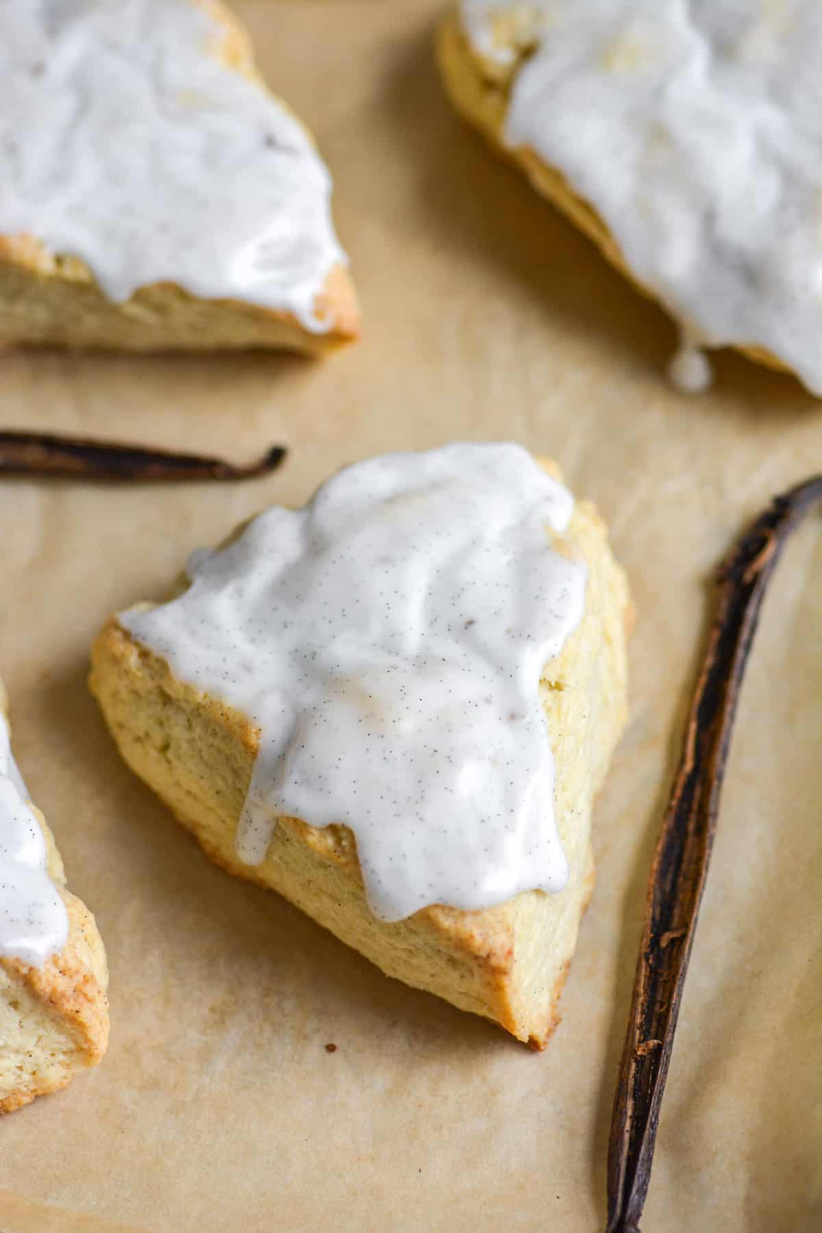 Vegan Vanilla Bean Scones on a parchment-lined baking sheet with vanilla beans in the scene.