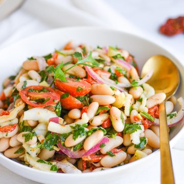 Bowl of white bean salad with a serving spoon
