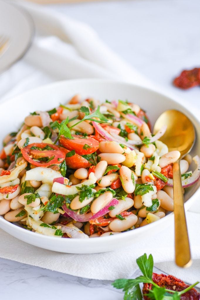 Bowl of vegan tuscan bean salad with a serving spoon