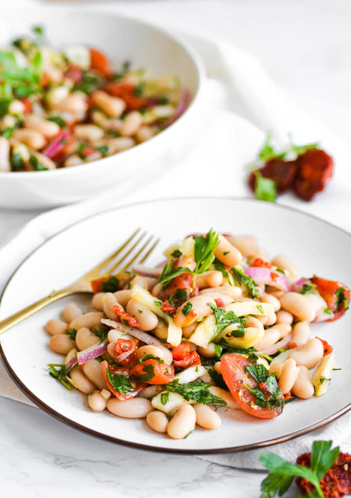 Two plates of vegan tuscan bean salad full of cannellini beans and tomatoes on a marble board