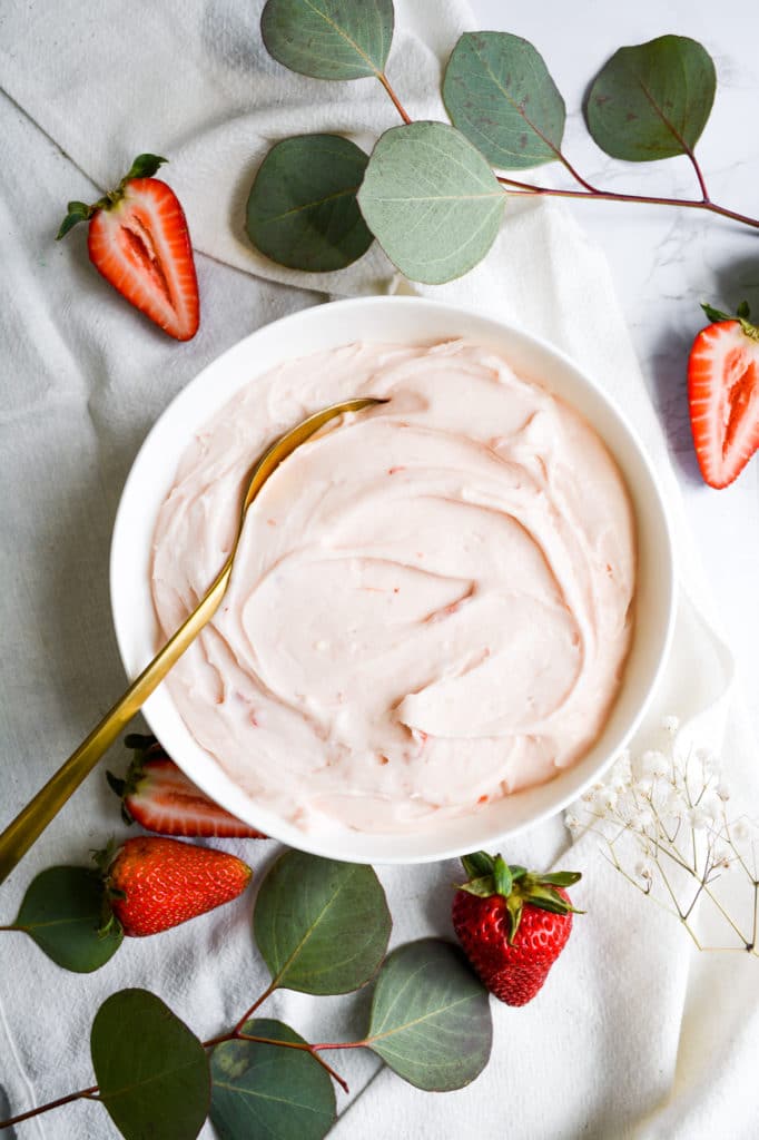 Bowl of strawberry cream cheese frosting with a gold spoon