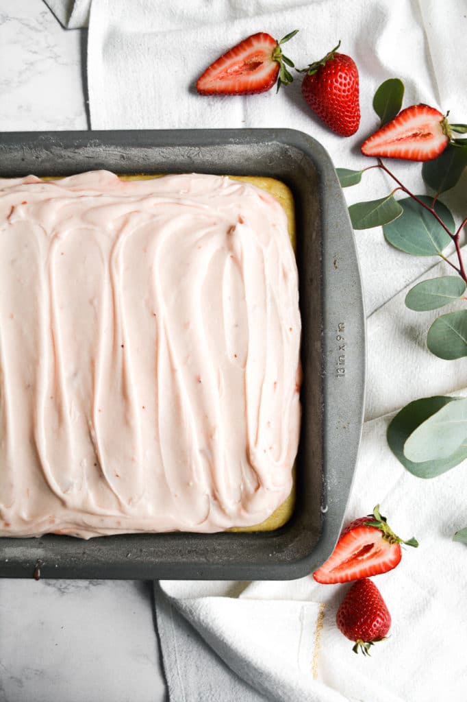 Vegan Lemon Cake with in a 9x13 pan on a white marble board with greenery and strawberries