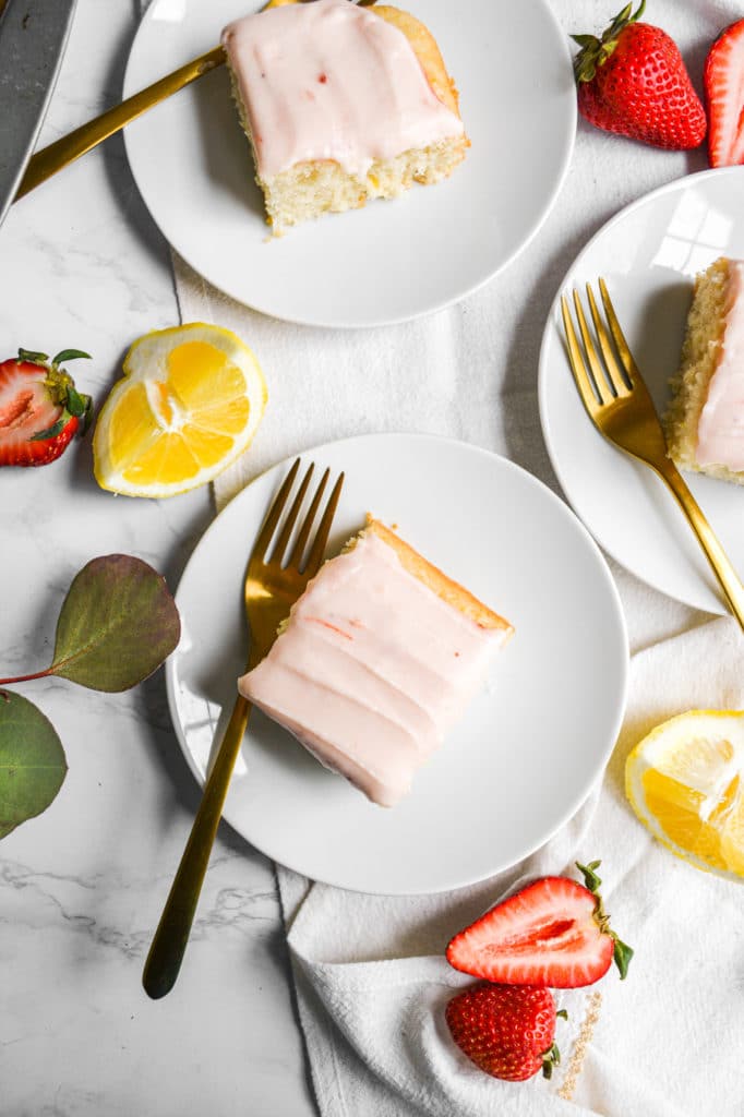 Overhead shot of 3 plates of lemon cake with cream cheese frosting with greenery and strawberries
