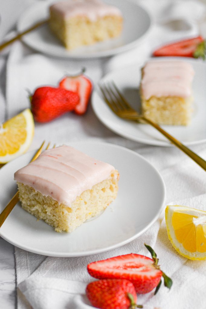 Portrait of 3 Pieces of Vegan Lemon cake on white plates with lemon wedges and strawberries