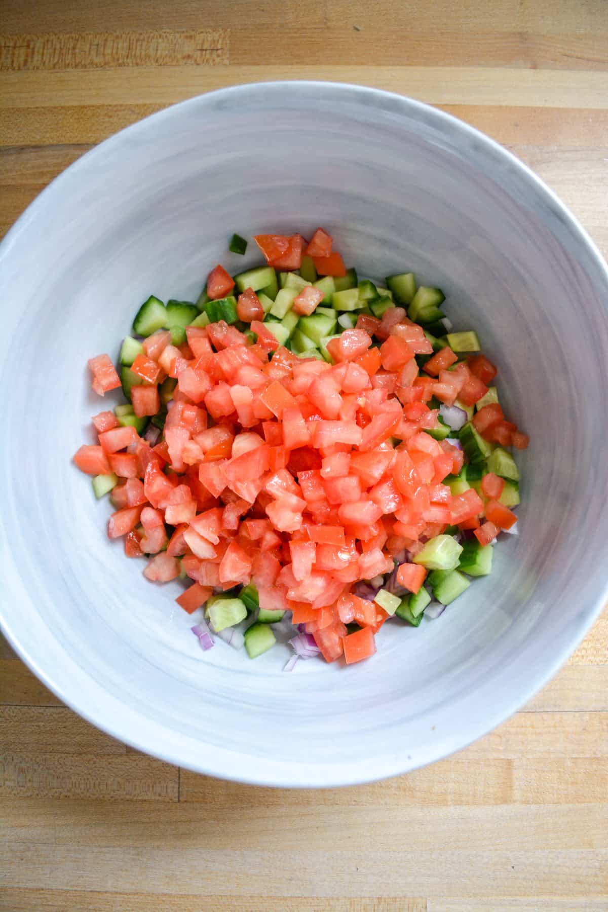 Cucumber, tomato and onion added to a large mixing bowl.