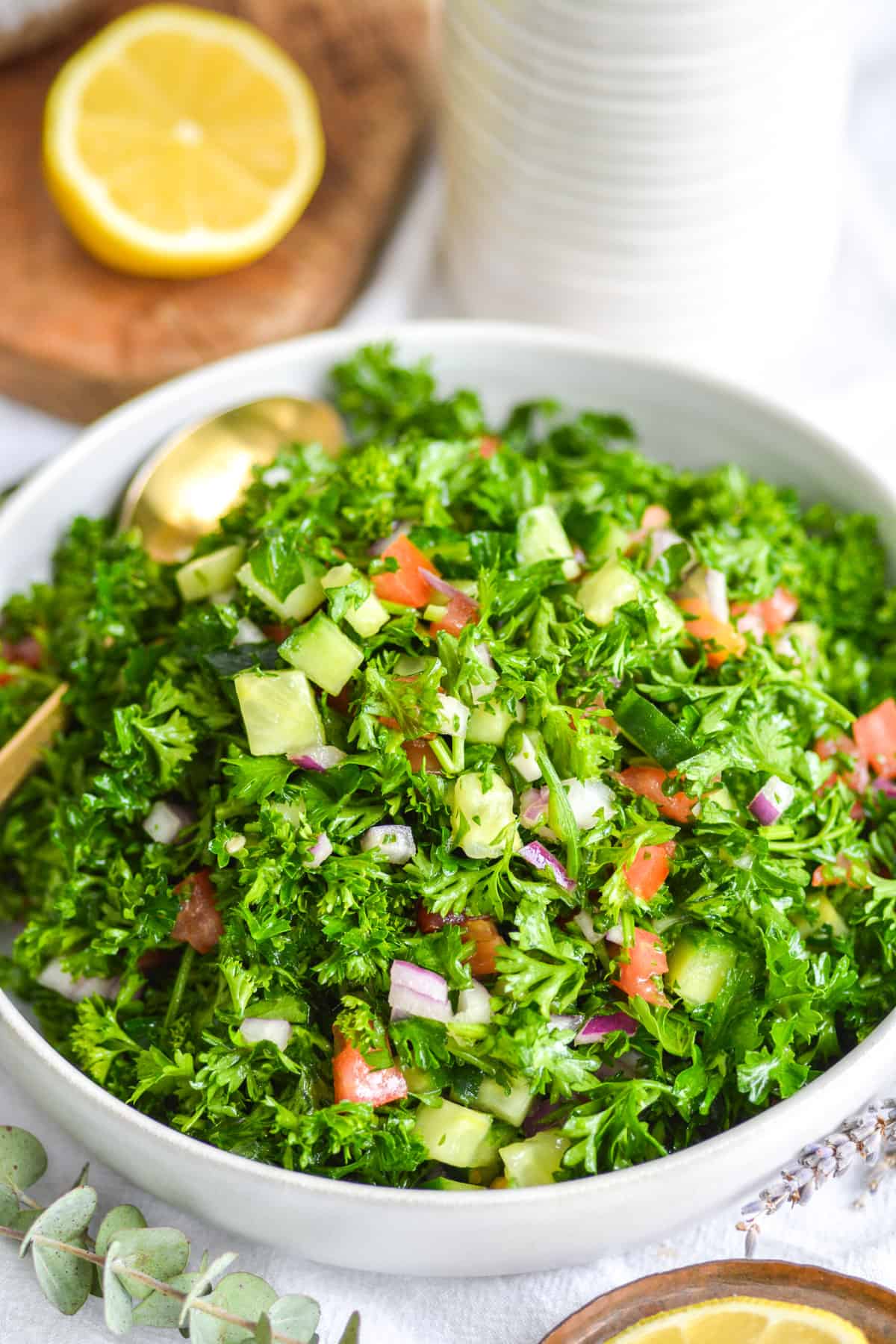 Grain-Free Tabbouleh Salad recipe in a white bowl on a white cloth with a lemon slice in the background.