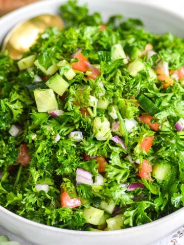 Grain-Free Tabouleh Salad in a white bowl with a gold spoon in it.