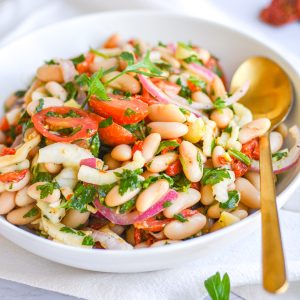 Tuscan cannellini bean salad in a white bowl with a gold spoon