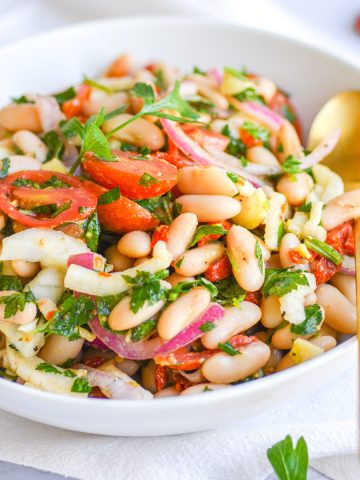 Tuscan cannellini bean salad in a white bowl with a gold spoon