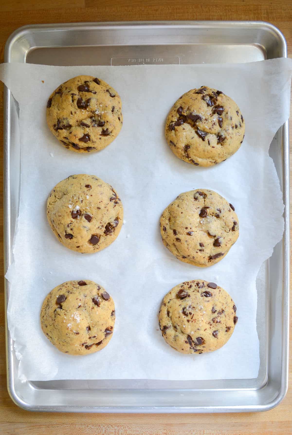 Levain Style Chocolate Chip Cookies on a baking tray that is lined with parchment