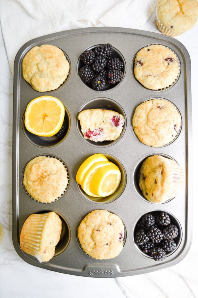 A muffin tin filled with vegan blackberry muffins, lemon slices and blackberries