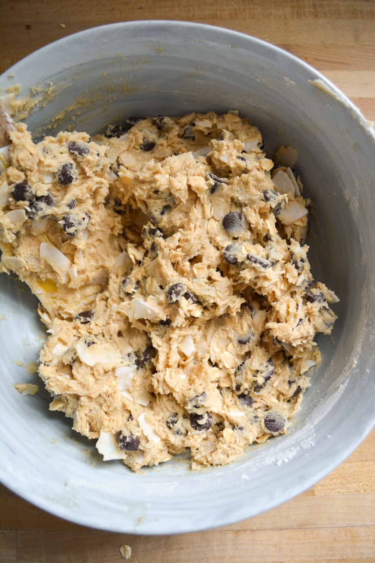 Coconut flakes and chocolate chips mixed into the oatmeal cookie dough in a mixing bowl.