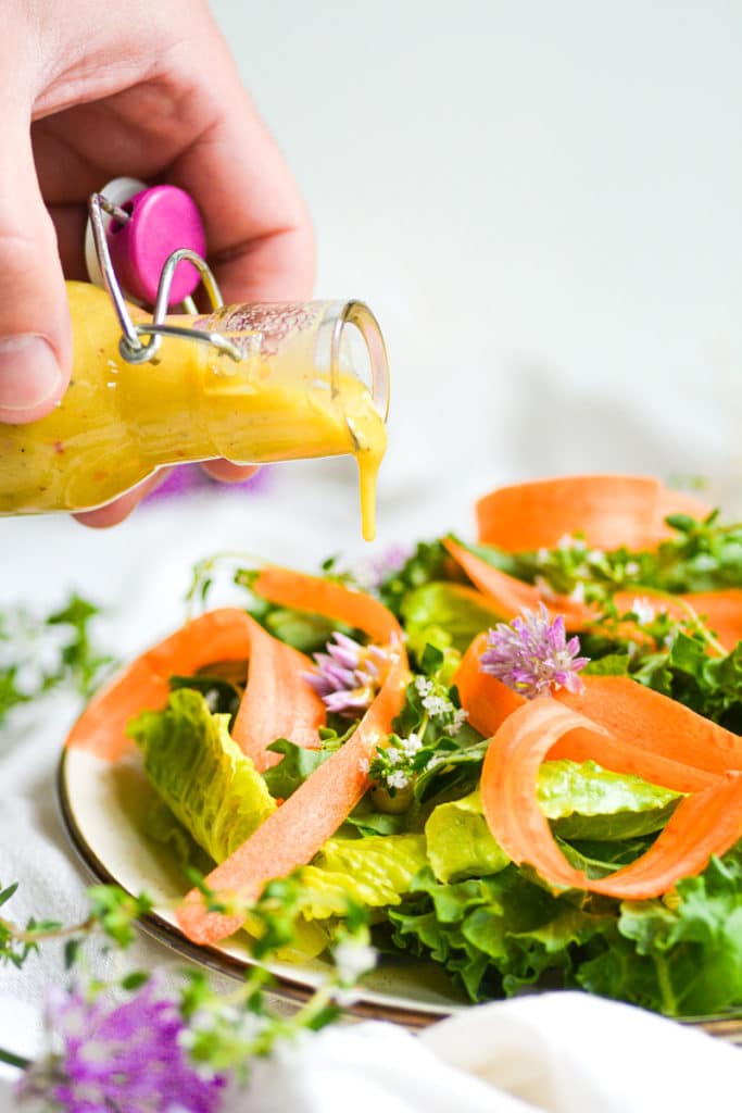 Hand holding a jar pouring honey mustard dressing onto salad