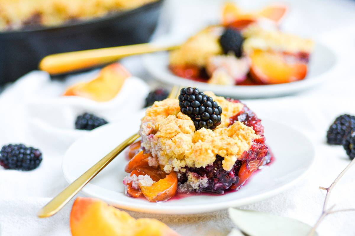 Peach blackberry cobbler on a white plate with a gold fork