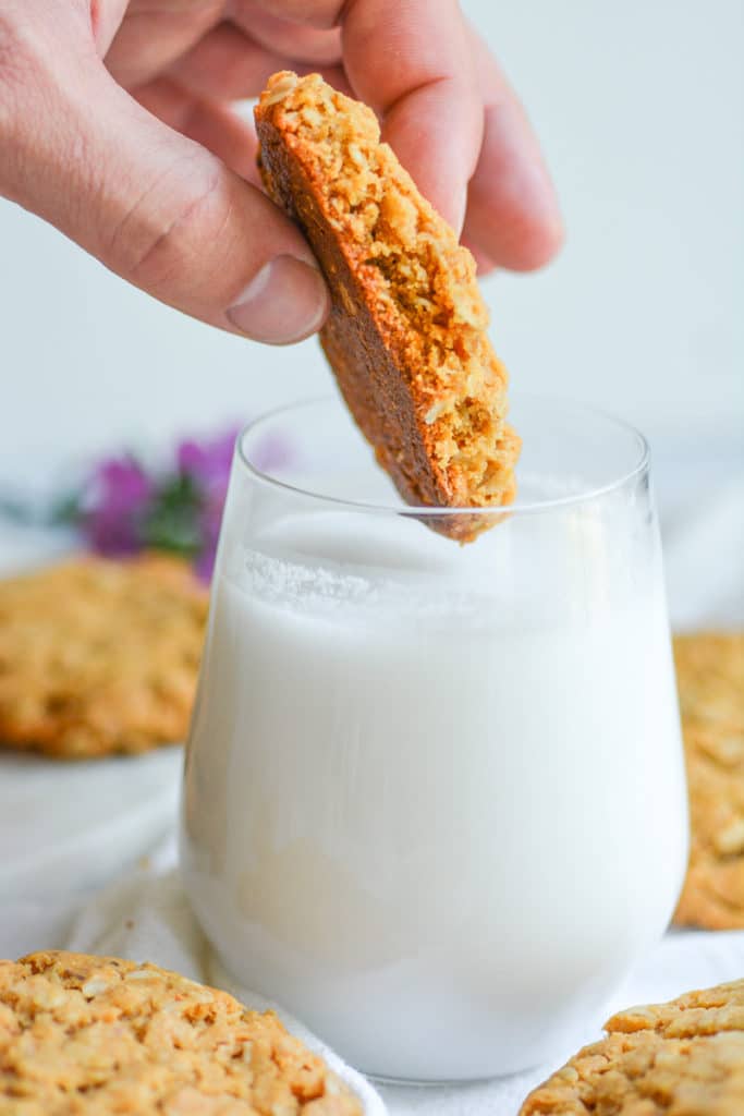 Hand dunking a Vegan Oatmeal peanut butter cookie into a glass of milk