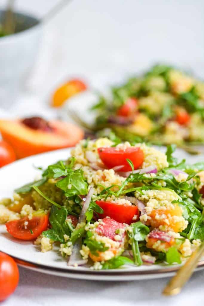 two plates of salad with peaches, tomatoes and arugula