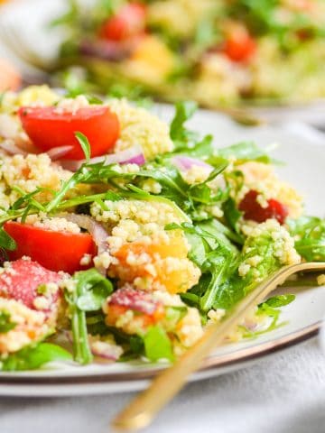 Close up of vegan couscous salad with nectarine and arugula on a plate with a gold fork