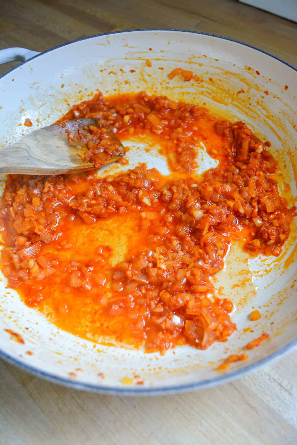 Vodka added into the onion and tomato paste mixture in a skillet with a wooden spoon on the top left.