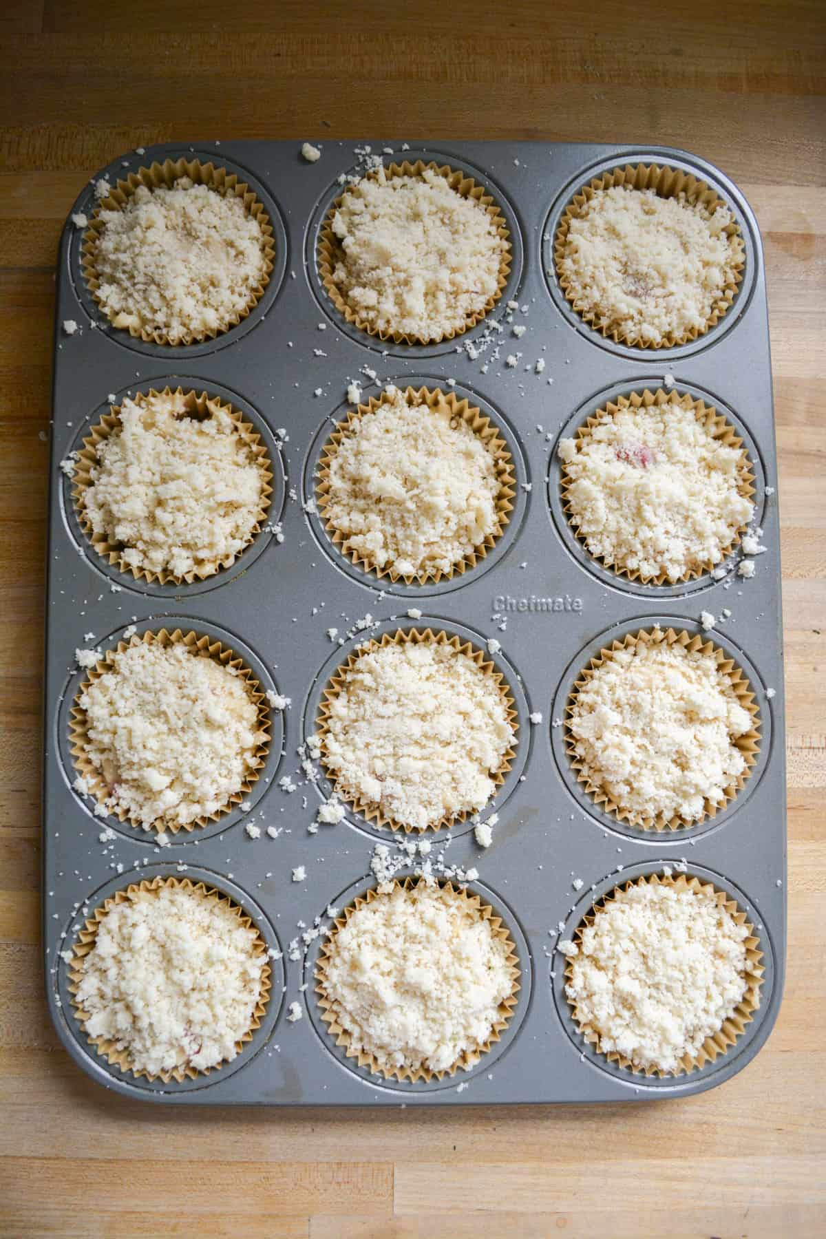 Muffin batter in a muffin tin topped with streusel.