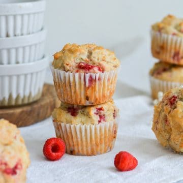 two vegan raspberry muffins with raspberries in the foreground