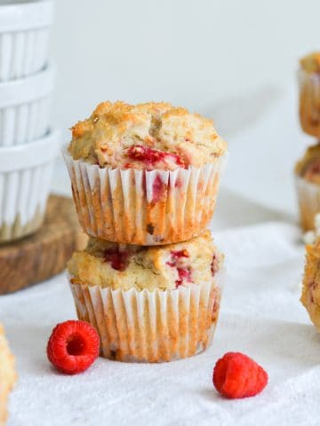 2 Vegan Raspberry Muffins stacked with fresh raspberries in the foreground