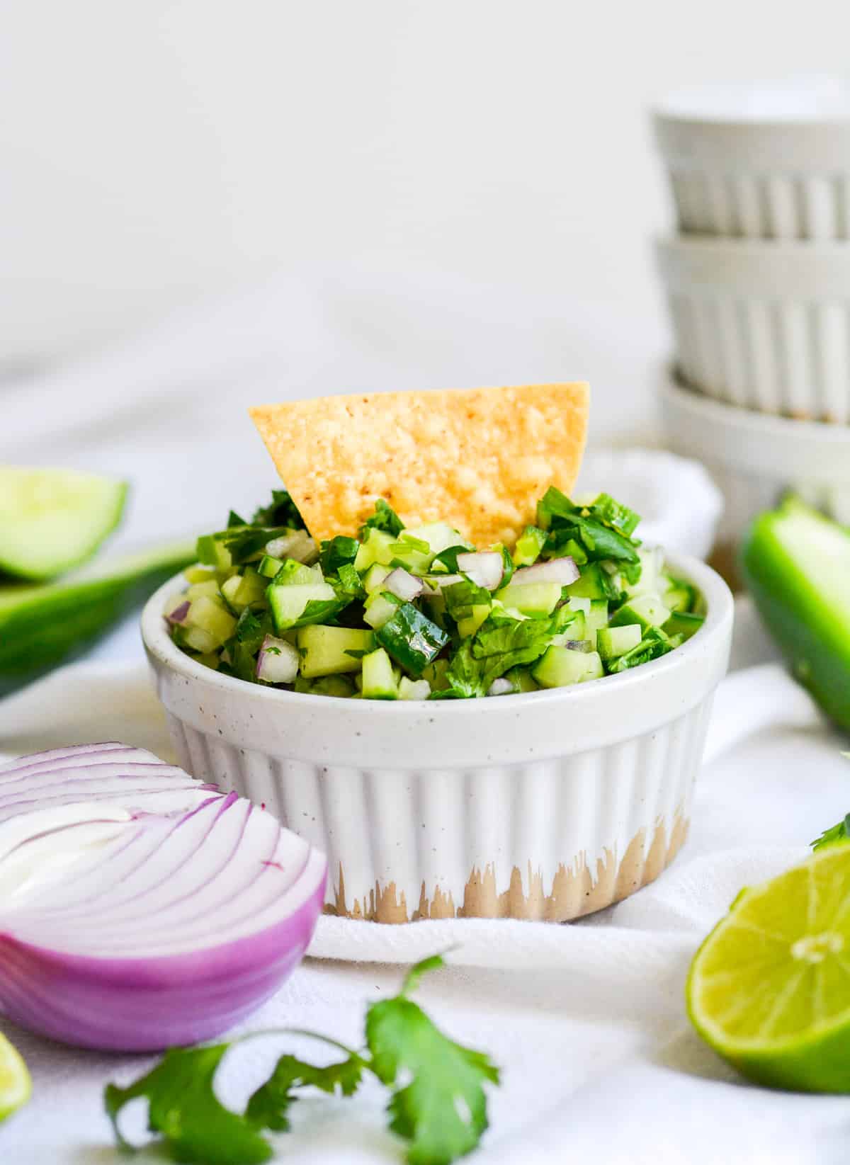 Cucumber pico de gallo in a ramekin with a tortilla chip sticking out of it
