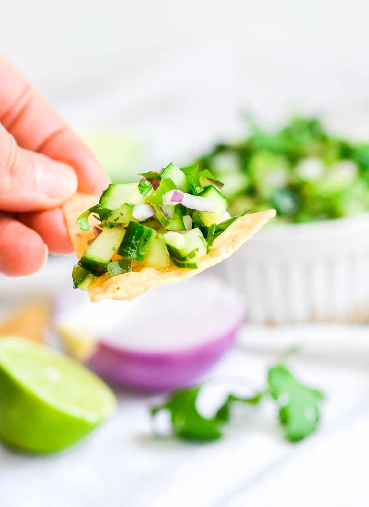 Hand holding a chip with cucumber pico de gallo on it