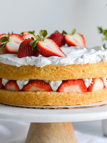 Vegan Strawberry Shortcake Cake on a cake stand with greenery in the background