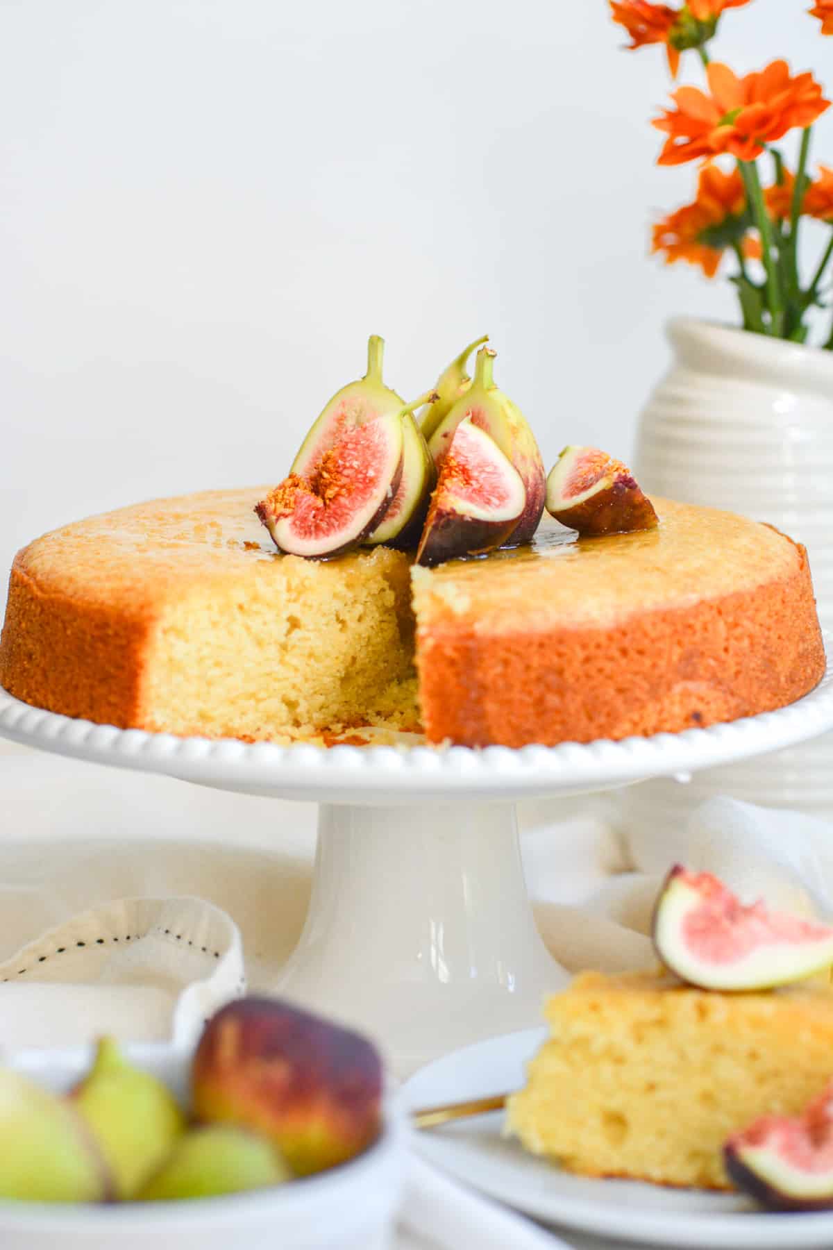 Vegan and Eggless Olive Oil Cake on a cake stand garnished with cardamom honey and figs