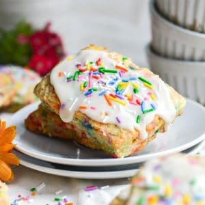 two birthday cake scones on a white plate with sprinkles on the table