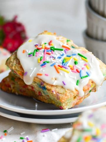 two birthday cake scones on a white plate with sprinkles on the table