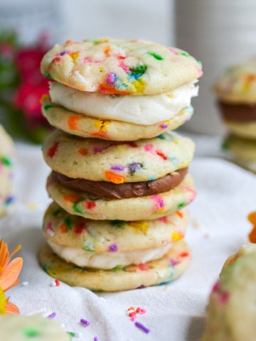 three funfetti sandwich cookies stacked on top of each other on a white cloth