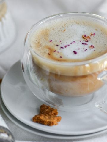 A cardamom late garnished with rose petals in a glass mug on a white plate