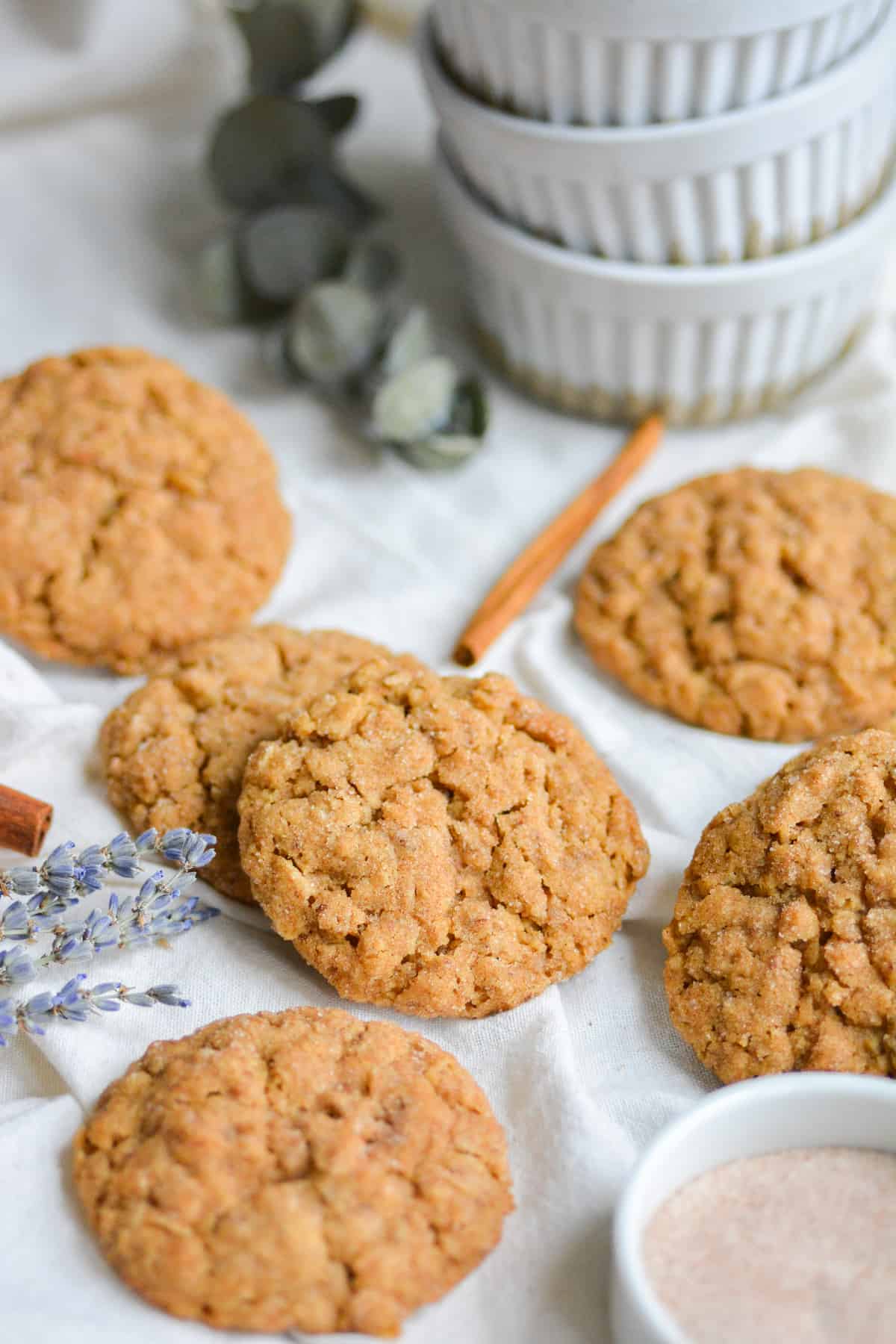 Oatmeal Snickerdoodle cookies on a white cloth with lavender flowers and cinnamon sticks around the scene.