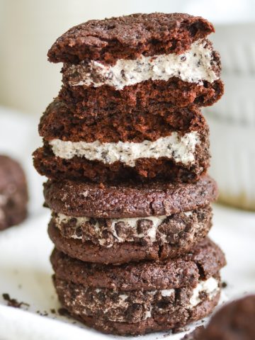 A stack of vegan oreo whoopie pies with one broken open to show the middle